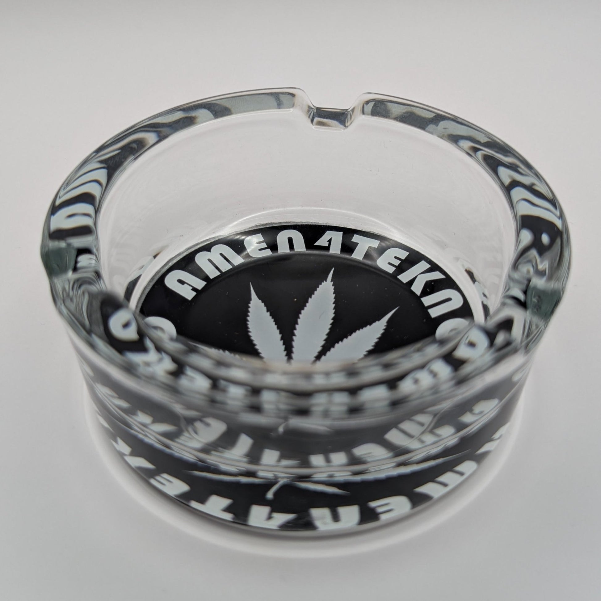 Glass ashtray with 'AMEN4TEKNO' branding on a white background